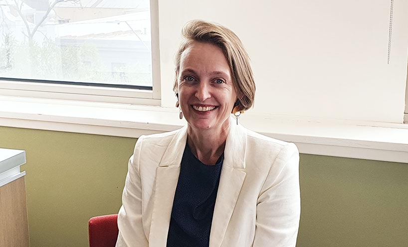 Sarah Austin smiling in front of window while wearing a white jacket and a black top.