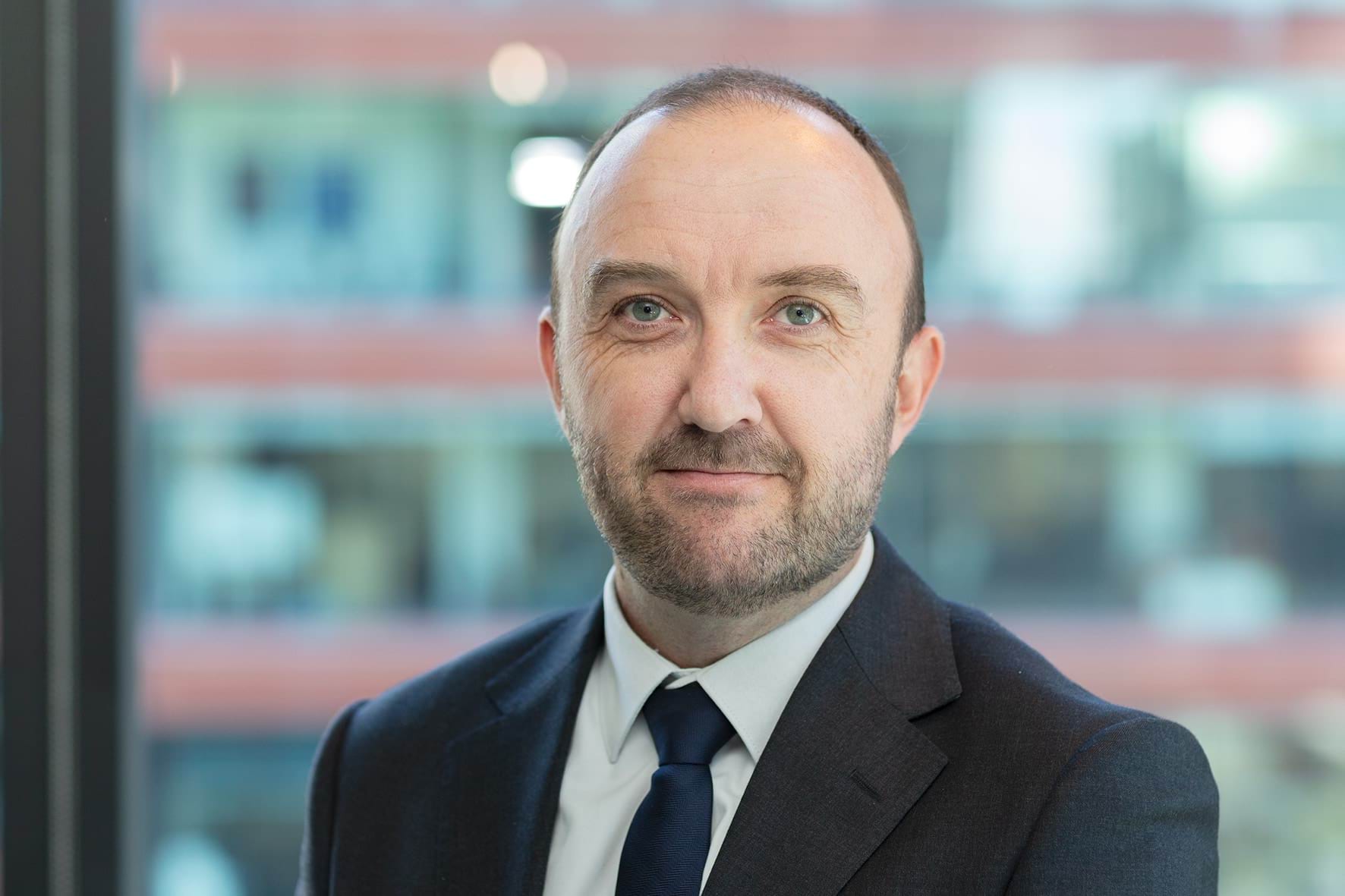 Profile photo of man with short hair wearing a suit and smiling at camera.