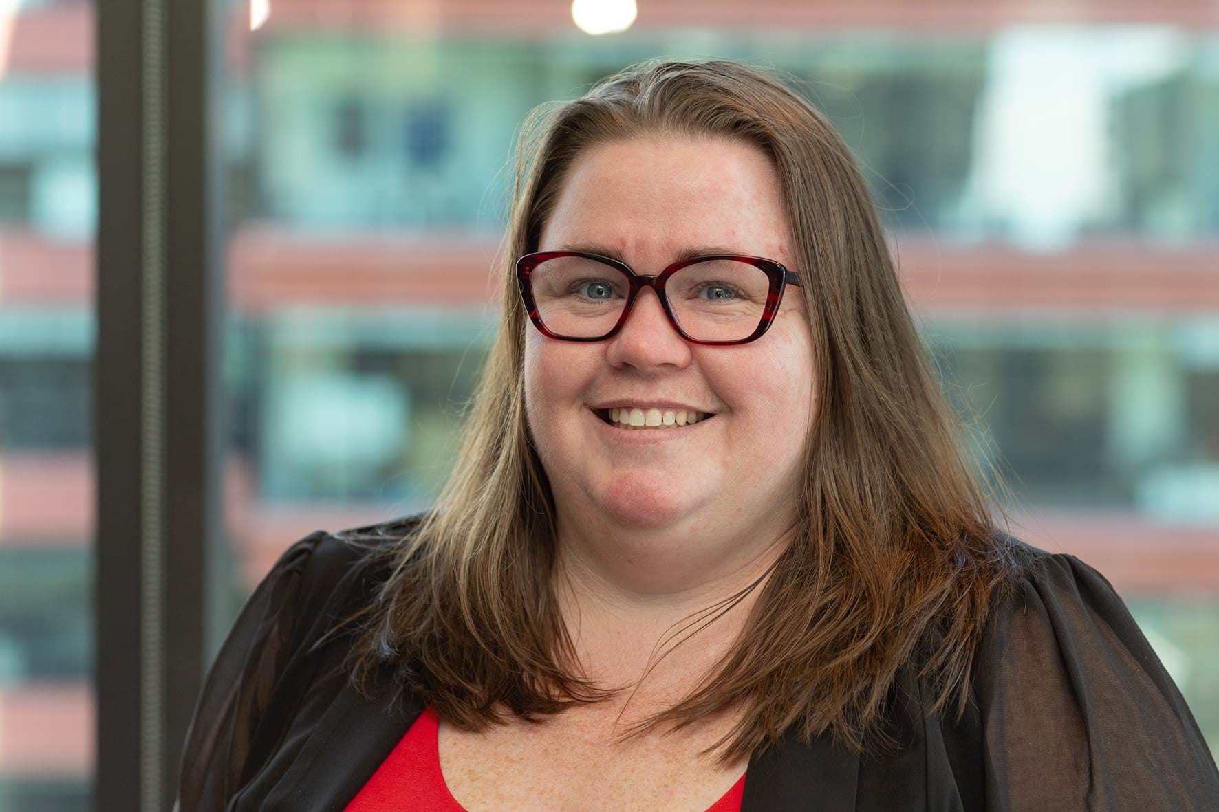 Profile photo of woman with long brown hair and glasses smiling at camera.