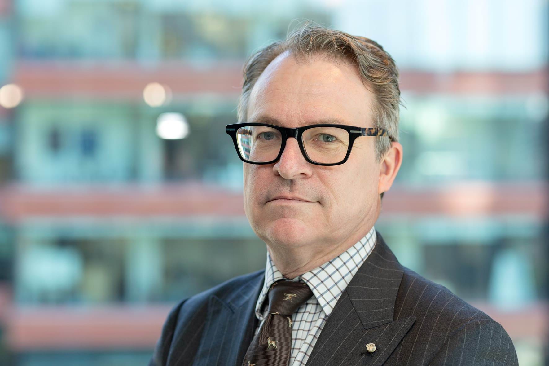 Profile photo of man in suit with short grey hair and glasses.