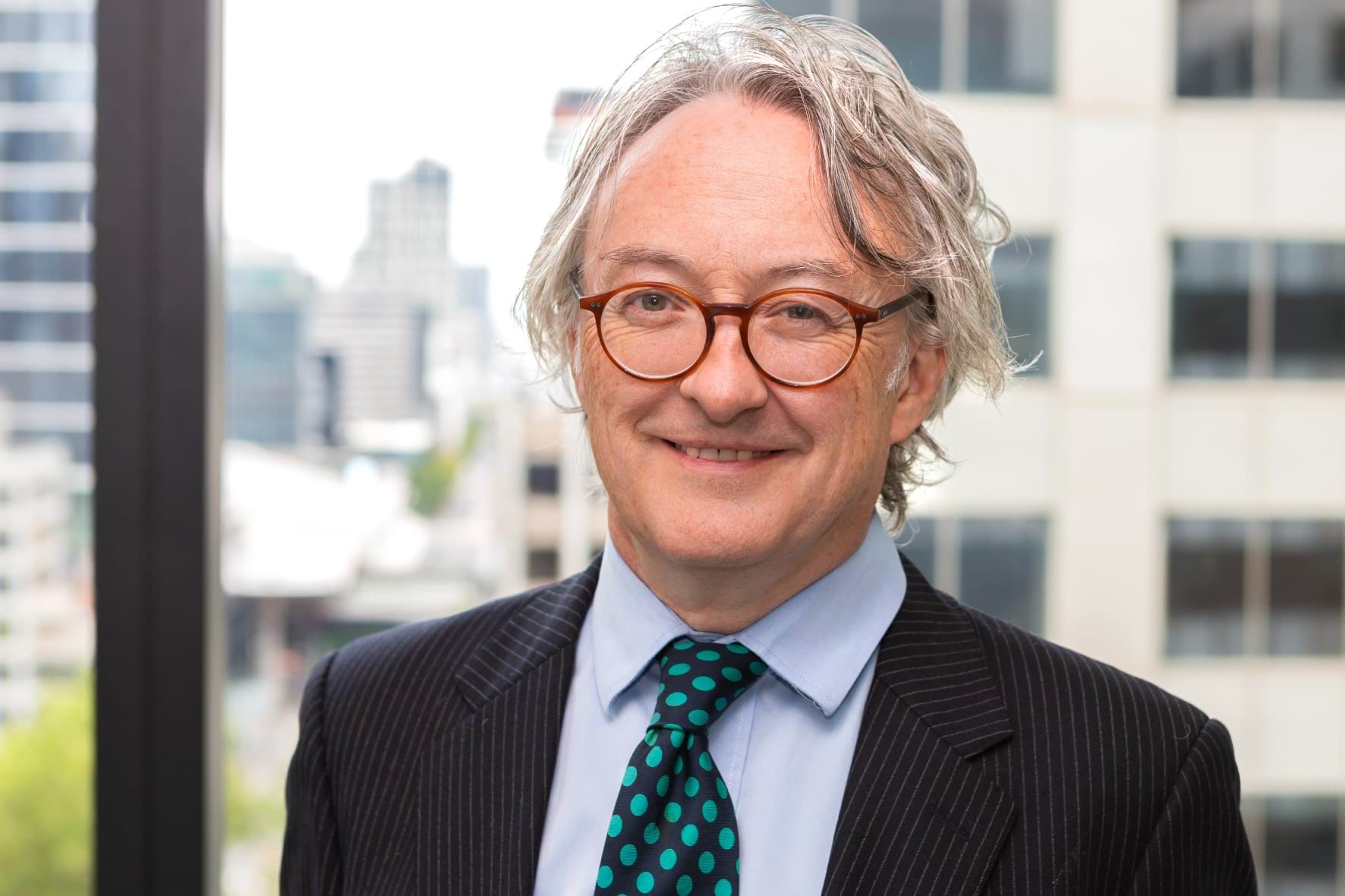 Profile photo of man with grey hair and glasses wearing a suit and smiling at camera.