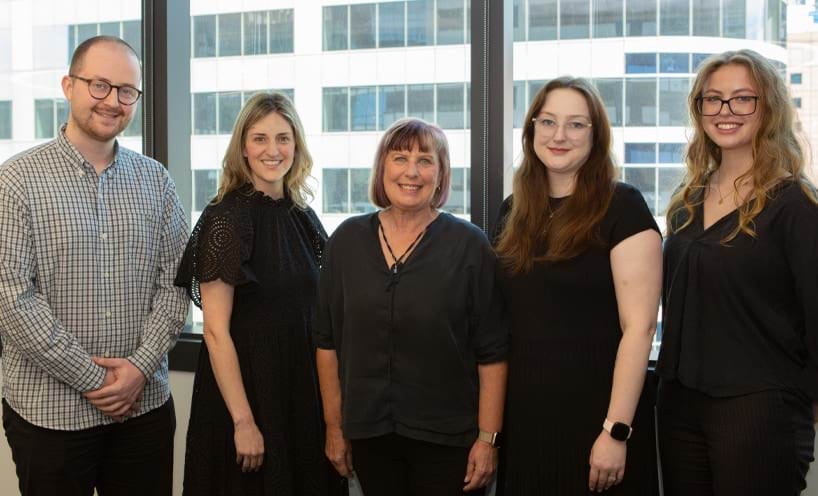 The five people who make up the Practitioner Support Officer team stand in a row, smiling towards the camera. 